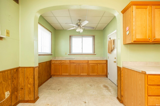 kitchen with a drop ceiling, wooden walls, and ceiling fan