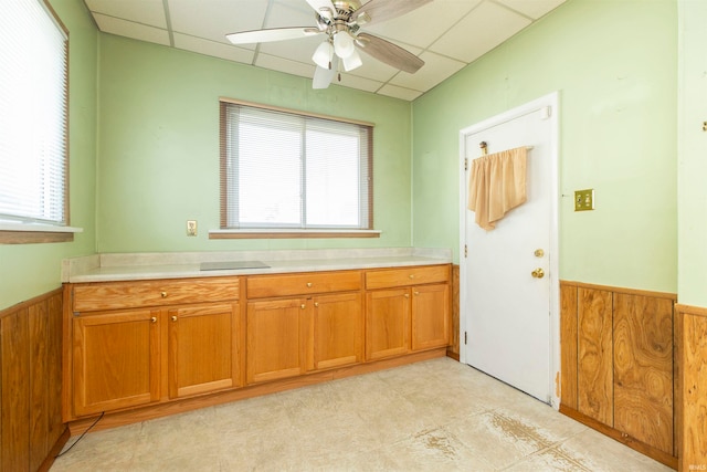 kitchen with ceiling fan, a paneled ceiling, light tile patterned floors, and wood walls