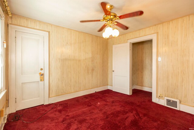 unfurnished room featuring dark carpet, wood walls, and ceiling fan