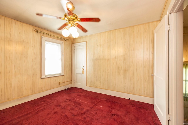 unfurnished room with carpet floors, wooden walls, and ceiling fan