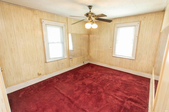 carpeted empty room featuring ceiling fan, a wealth of natural light, and wooden walls