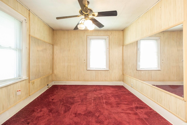 carpeted spare room with ceiling fan, a wealth of natural light, and wooden walls