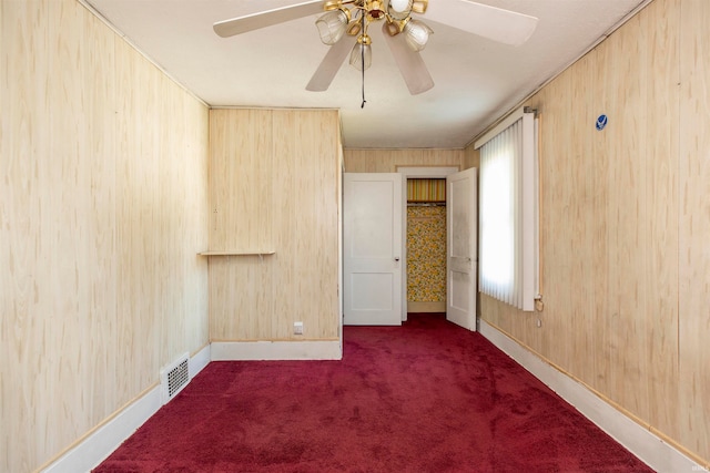 spare room featuring ceiling fan, wooden walls, and dark colored carpet