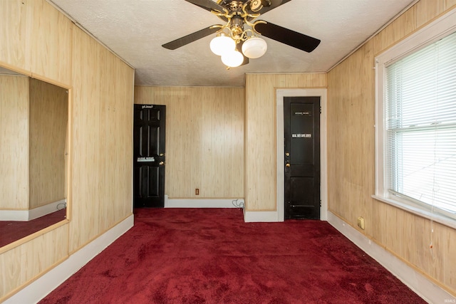 unfurnished room featuring a textured ceiling, wooden walls, dark carpet, and ceiling fan