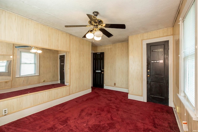 carpeted empty room featuring wooden walls, a textured ceiling, and ceiling fan