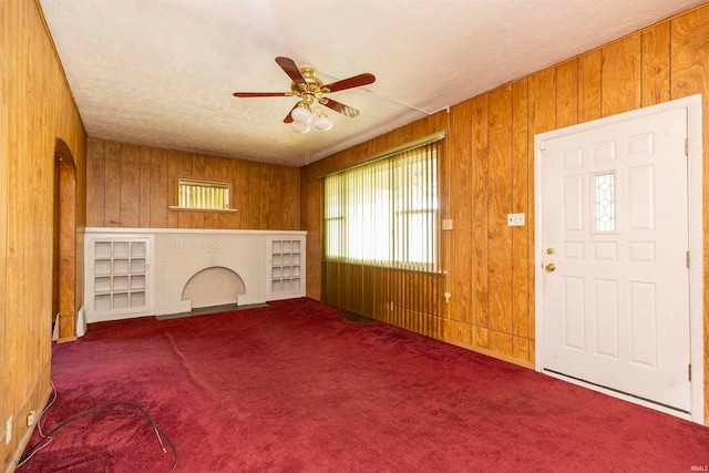 interior space featuring carpet floors, wooden walls, and ceiling fan