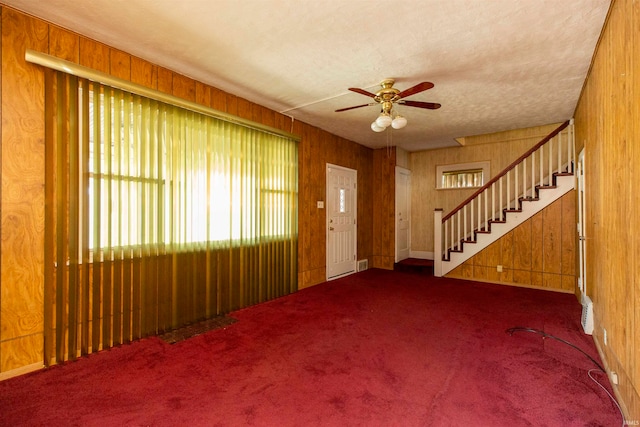 interior space featuring carpet floors, wooden walls, and ceiling fan