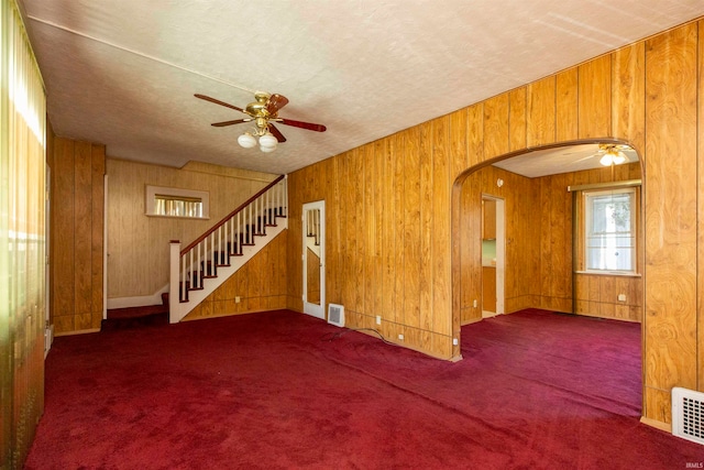 empty room with wood walls, dark carpet, and ceiling fan