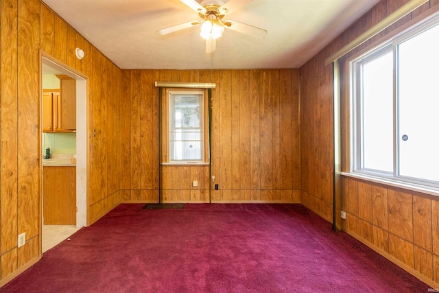 carpeted empty room featuring wooden walls, ceiling fan, and plenty of natural light