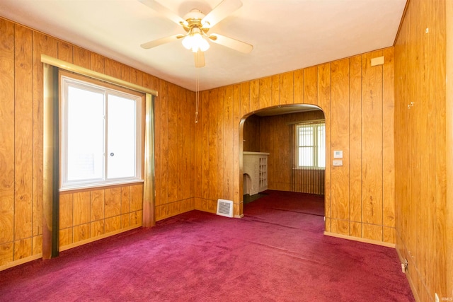 carpeted empty room featuring ceiling fan, a healthy amount of sunlight, and wood walls