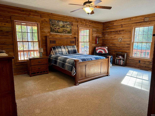 carpeted bedroom with ceiling fan, wood walls, and multiple windows