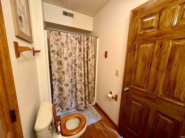bathroom with a textured ceiling, hardwood / wood-style flooring, toilet, and walk in shower