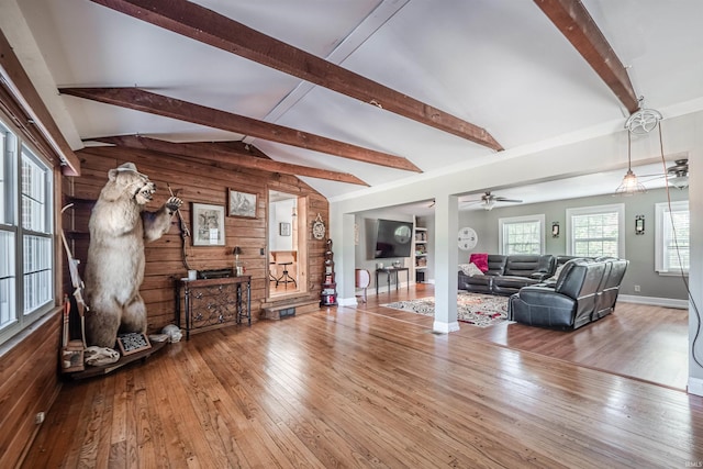 living room featuring ceiling fan, vaulted ceiling with beams, wood-type flooring, and wood walls