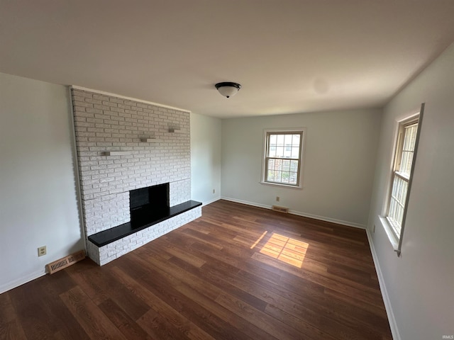 unfurnished living room with a brick fireplace and dark hardwood / wood-style flooring