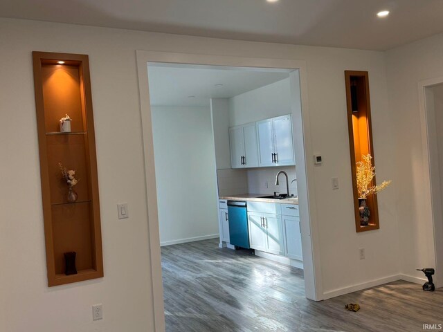 kitchen featuring sink, dishwasher, white cabinetry, and wood-type flooring