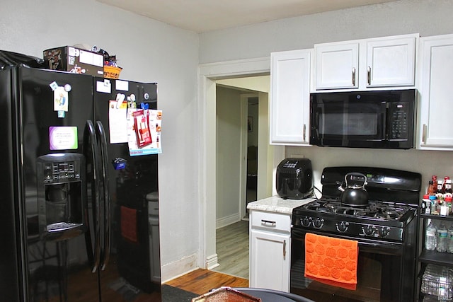 kitchen with white cabinetry, light stone countertops, black appliances, and hardwood / wood-style floors