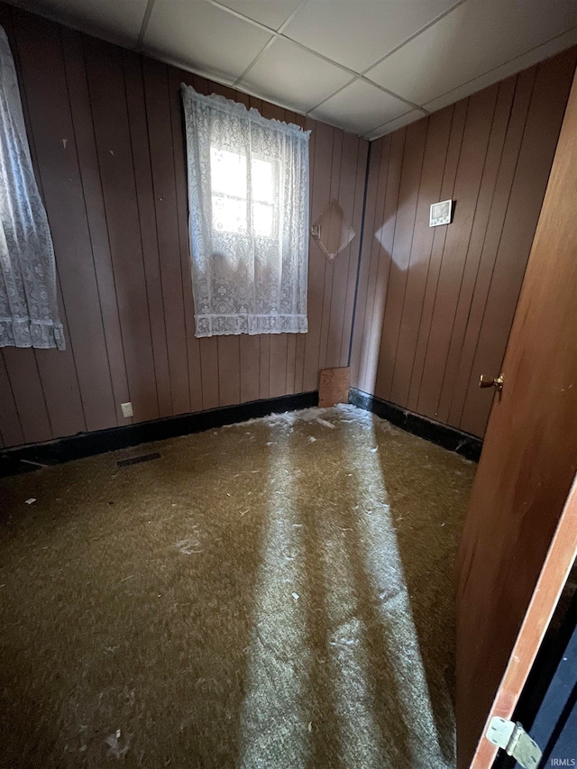 spare room with a drop ceiling and wood walls