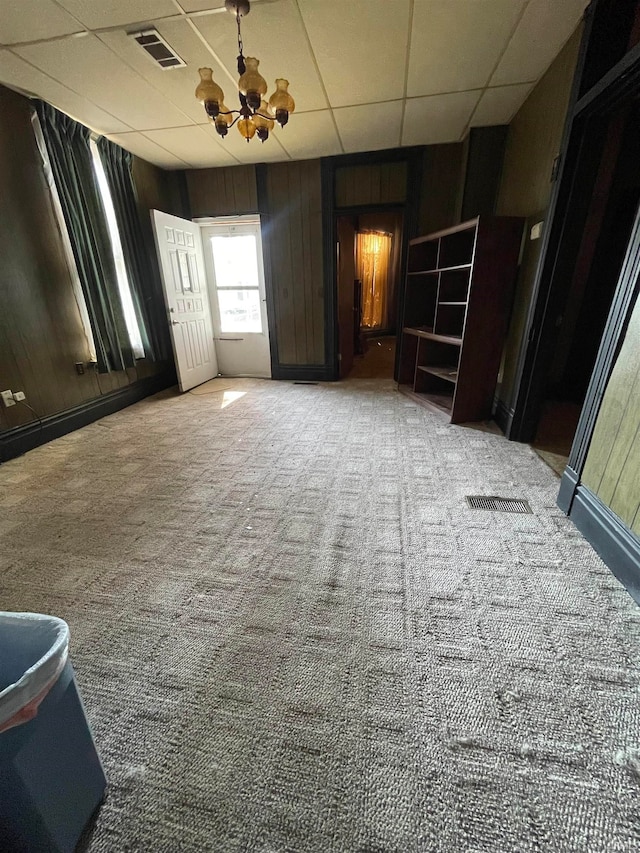 carpeted empty room featuring a drop ceiling and wood walls