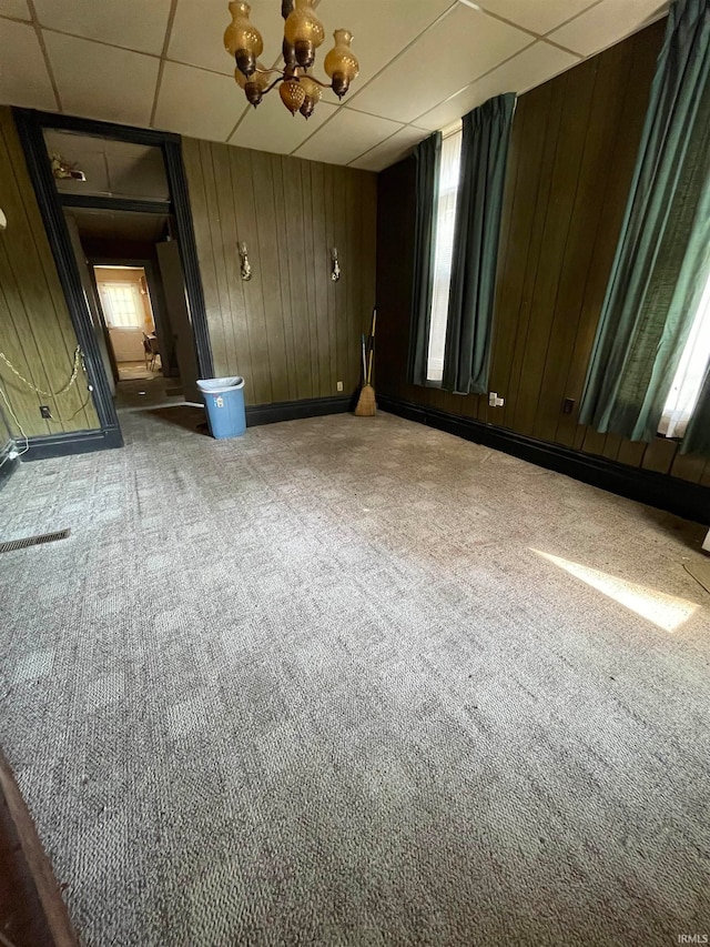 carpeted empty room featuring a paneled ceiling and wood walls