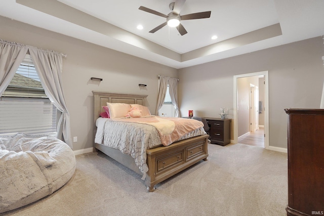 carpeted bedroom featuring a raised ceiling, multiple windows, and ceiling fan