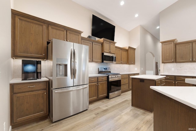 kitchen with a kitchen island, decorative backsplash, light wood-type flooring, appliances with stainless steel finishes, and high vaulted ceiling