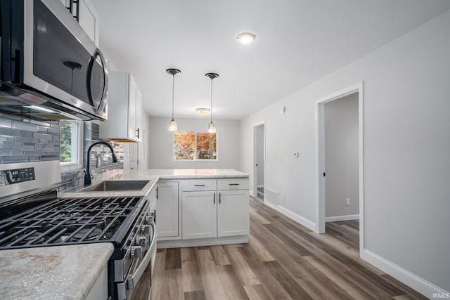 kitchen featuring wood-type flooring, sink, stainless steel appliances, white cabinets, and decorative backsplash