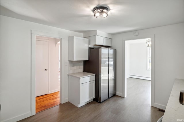 kitchen featuring decorative backsplash, baseboard heating, white cabinets, light hardwood / wood-style floors, and stainless steel refrigerator