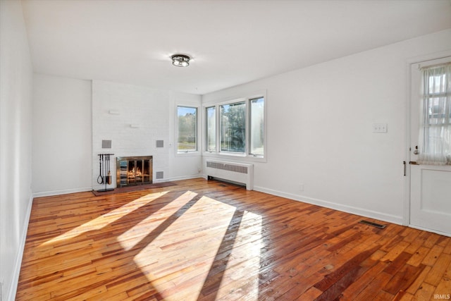 unfurnished living room with light hardwood / wood-style floors, radiator, and a brick fireplace