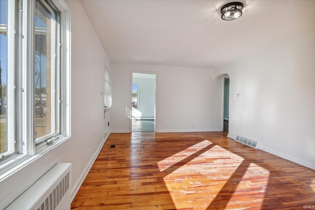 unfurnished room featuring baseboard heating, hardwood / wood-style flooring, and radiator heating unit