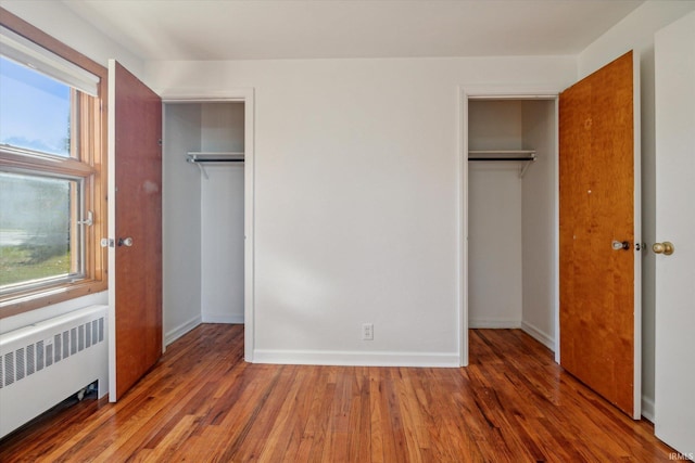 unfurnished bedroom with multiple windows, hardwood / wood-style floors, multiple closets, and radiator