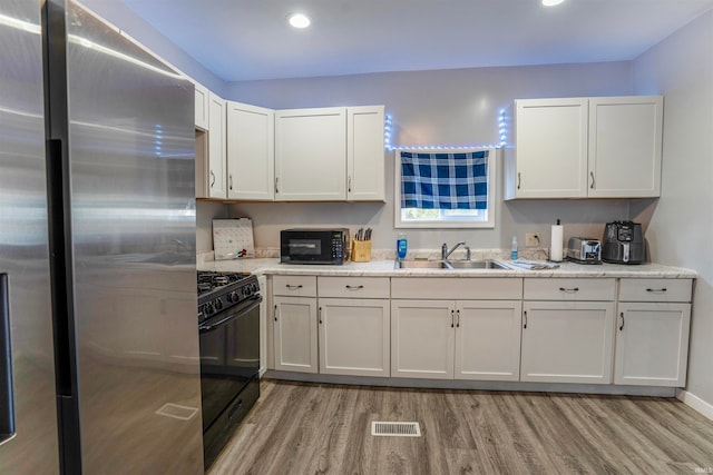 kitchen with sink, black appliances, white cabinetry, and light hardwood / wood-style floors