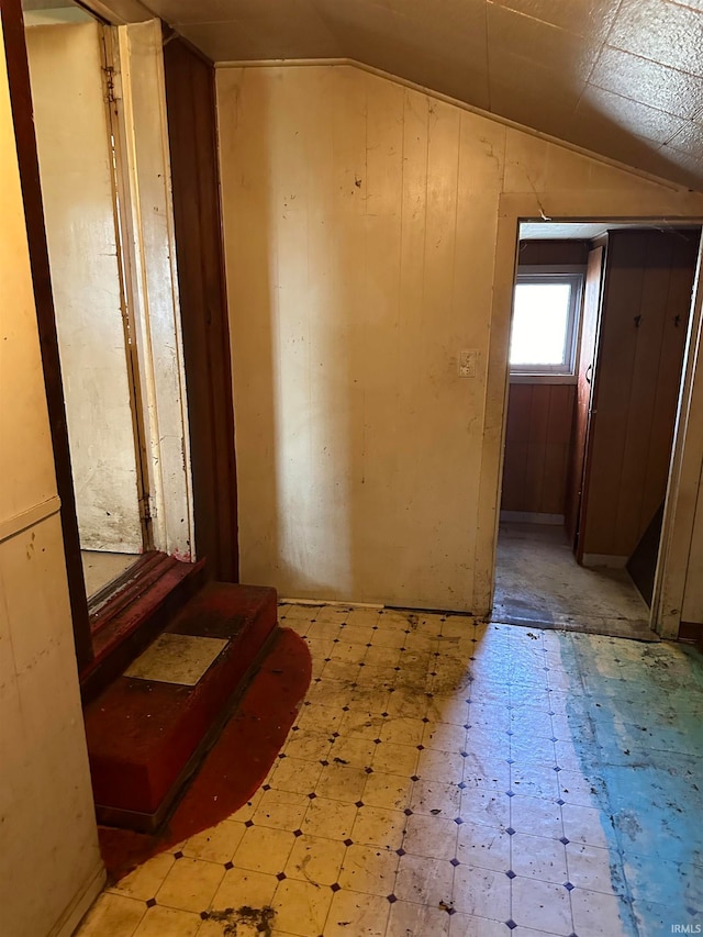 corridor featuring lofted ceiling and wooden walls