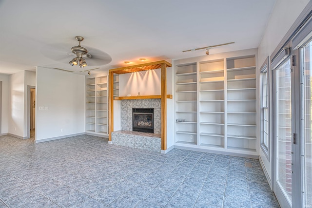 unfurnished living room featuring built in shelves, track lighting, a tiled fireplace, and ceiling fan