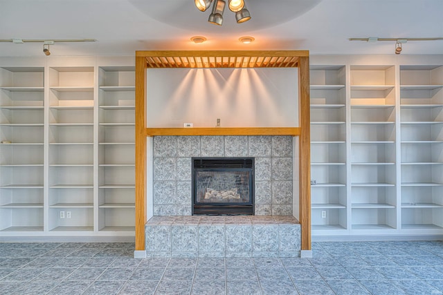 unfurnished living room with a tiled fireplace and rail lighting