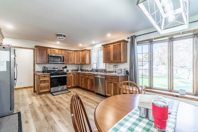 kitchen with appliances with stainless steel finishes, light stone countertops, light wood-type flooring, and a wealth of natural light