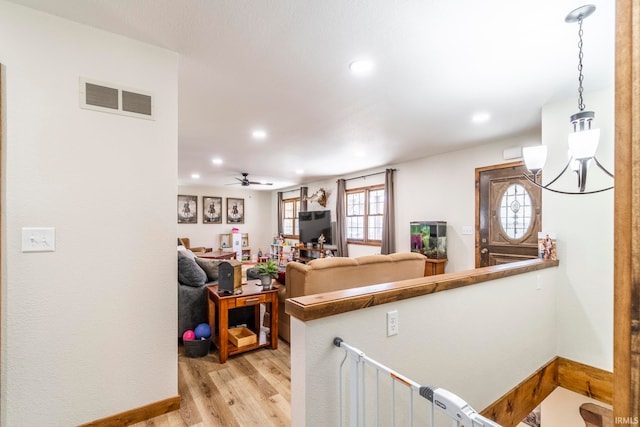 interior space with ceiling fan with notable chandelier and light wood-type flooring