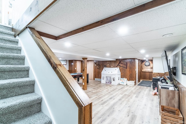 basement featuring light hardwood / wood-style flooring, a paneled ceiling, and wood walls