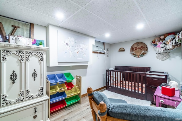 bedroom with light hardwood / wood-style floors, a drop ceiling, and a nursery area