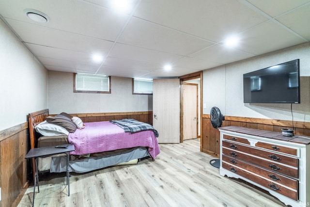 bedroom featuring wood walls, light hardwood / wood-style flooring, and a drop ceiling