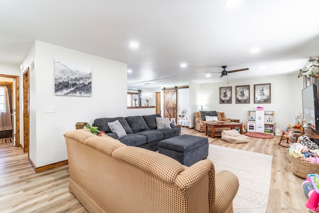 living room with a barn door, light wood-type flooring, and ceiling fan