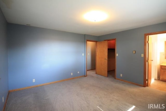 unfurnished bedroom with a spacious closet, a closet, ensuite bath, and light colored carpet