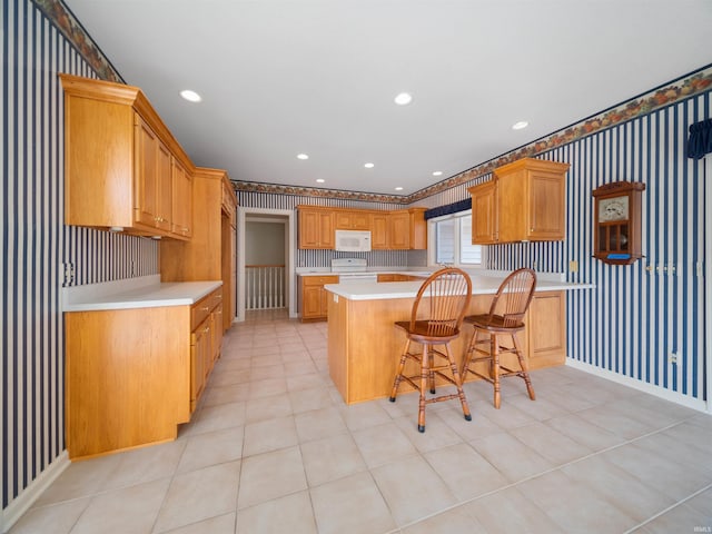 kitchen with a kitchen breakfast bar, kitchen peninsula, a center island, and white appliances