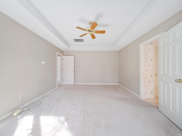 carpeted spare room with a raised ceiling and ceiling fan