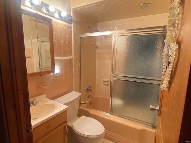 full bathroom with tile walls, vanity, toilet, and bath / shower combo with glass door