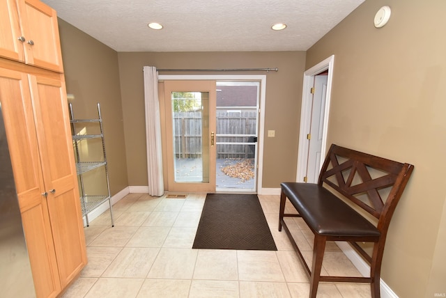 doorway to outside with a textured ceiling and light tile patterned floors