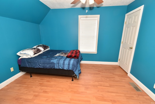 bedroom with lofted ceiling, a textured ceiling, light hardwood / wood-style floors, and ceiling fan