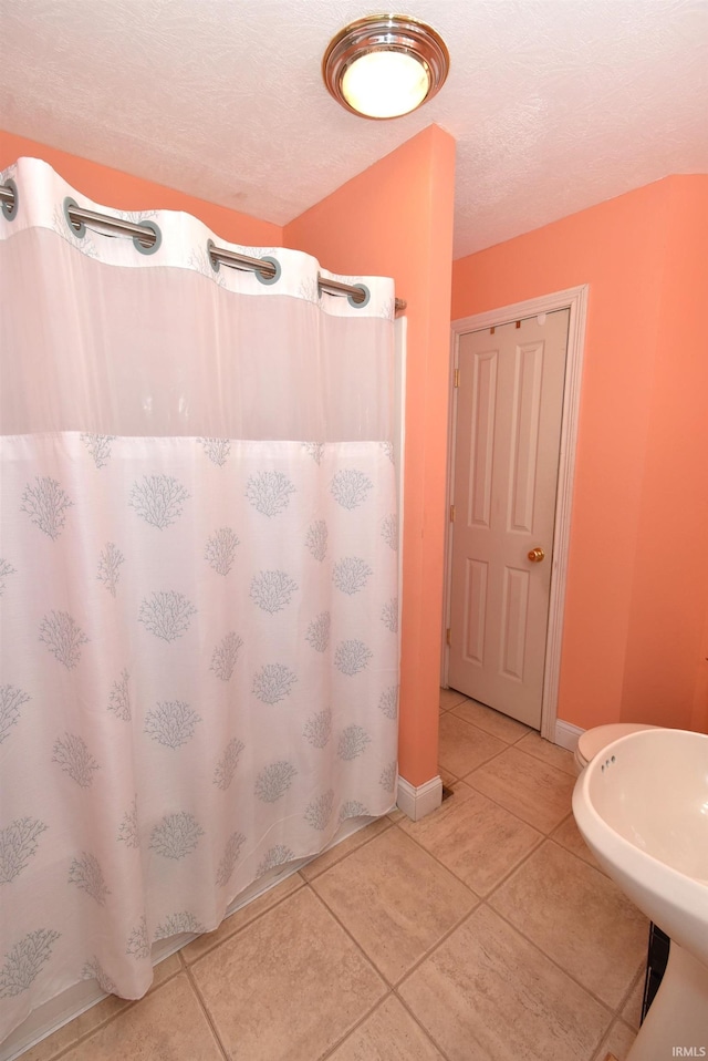 bathroom with a textured ceiling, curtained shower, sink, and tile patterned flooring