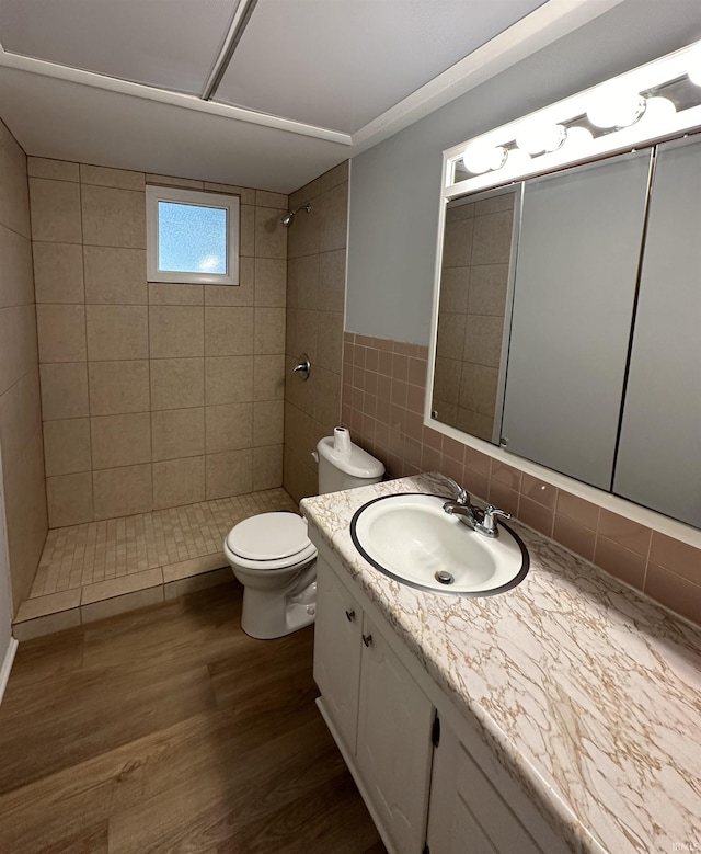 bathroom with hardwood / wood-style flooring, tile walls, toilet, tiled shower, and vanity