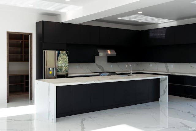 kitchen featuring sink, a spacious island, backsplash, stainless steel fridge, and wall chimney exhaust hood