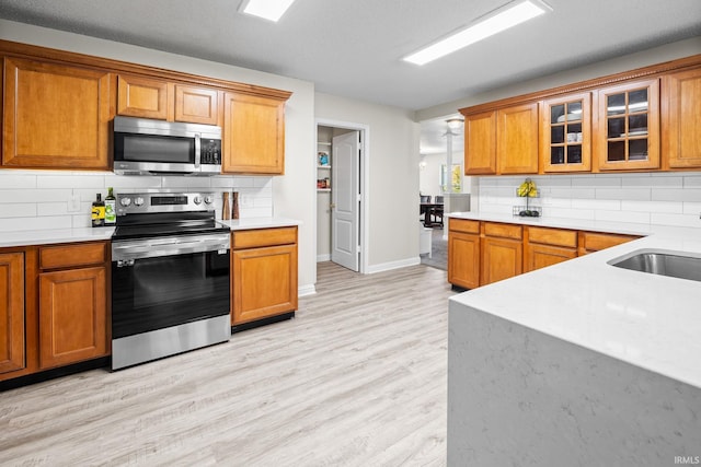 kitchen with backsplash, appliances with stainless steel finishes, sink, and light hardwood / wood-style floors